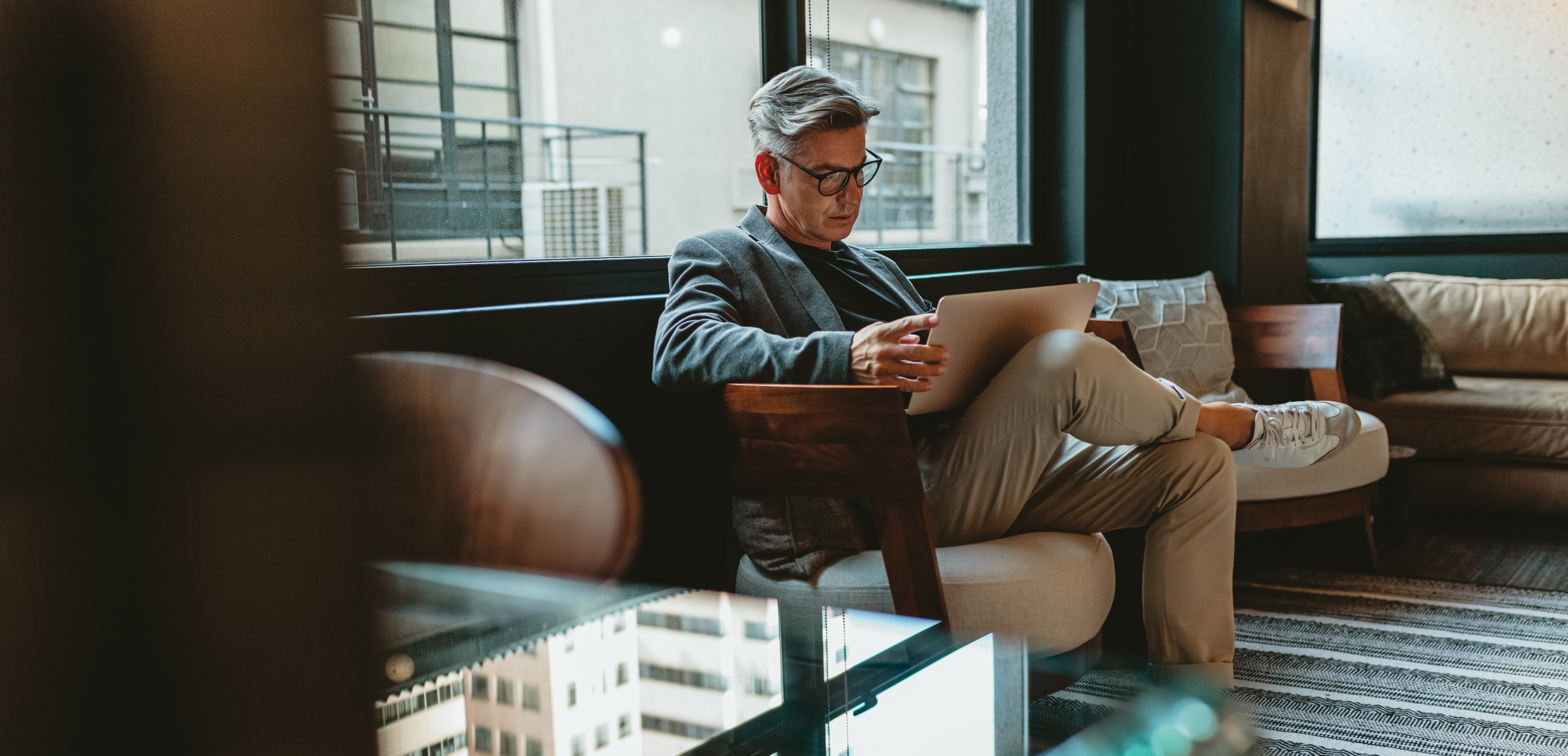Homem de óculos sentado em uma poltrona moderna em um ambiente corporativo, usando um laptop.
